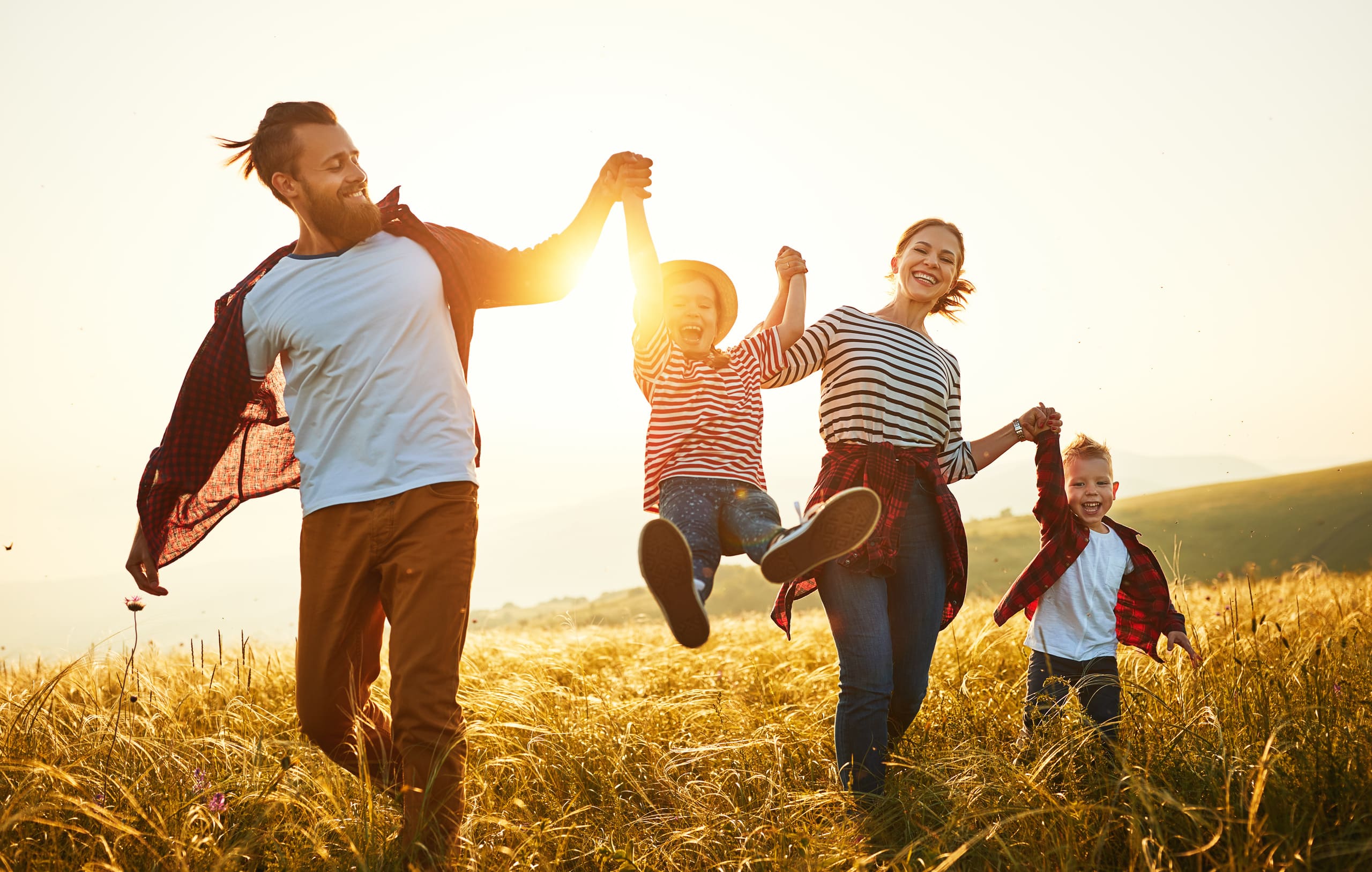 Familie läuft bei teifstehender Sonne über hohe Wiese